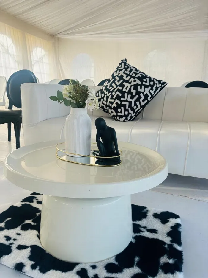 A white sofa styled with a black and white patterned cushion and a side table with a gold tray on a cowhide rug