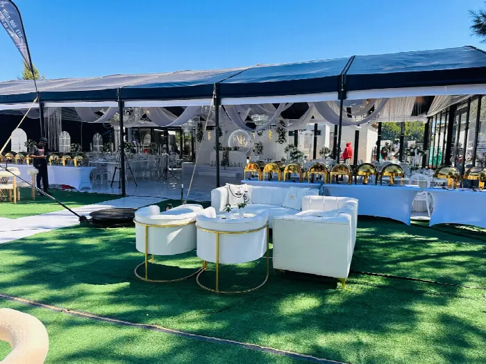 An outdoor marquee set for a function, with gold chafing dishes along the buffet and white lounge seating on the lawn
