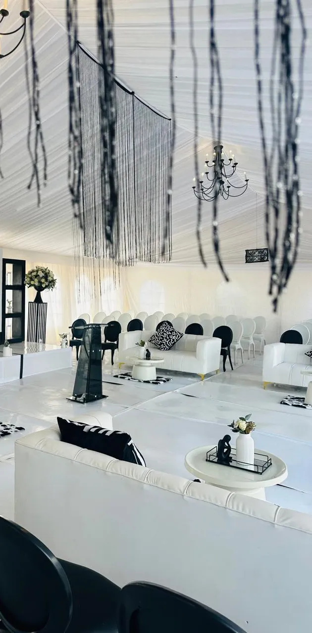 The interior of a memorial tent styled in black and white with beaded draping, chandeliers and lounge seating